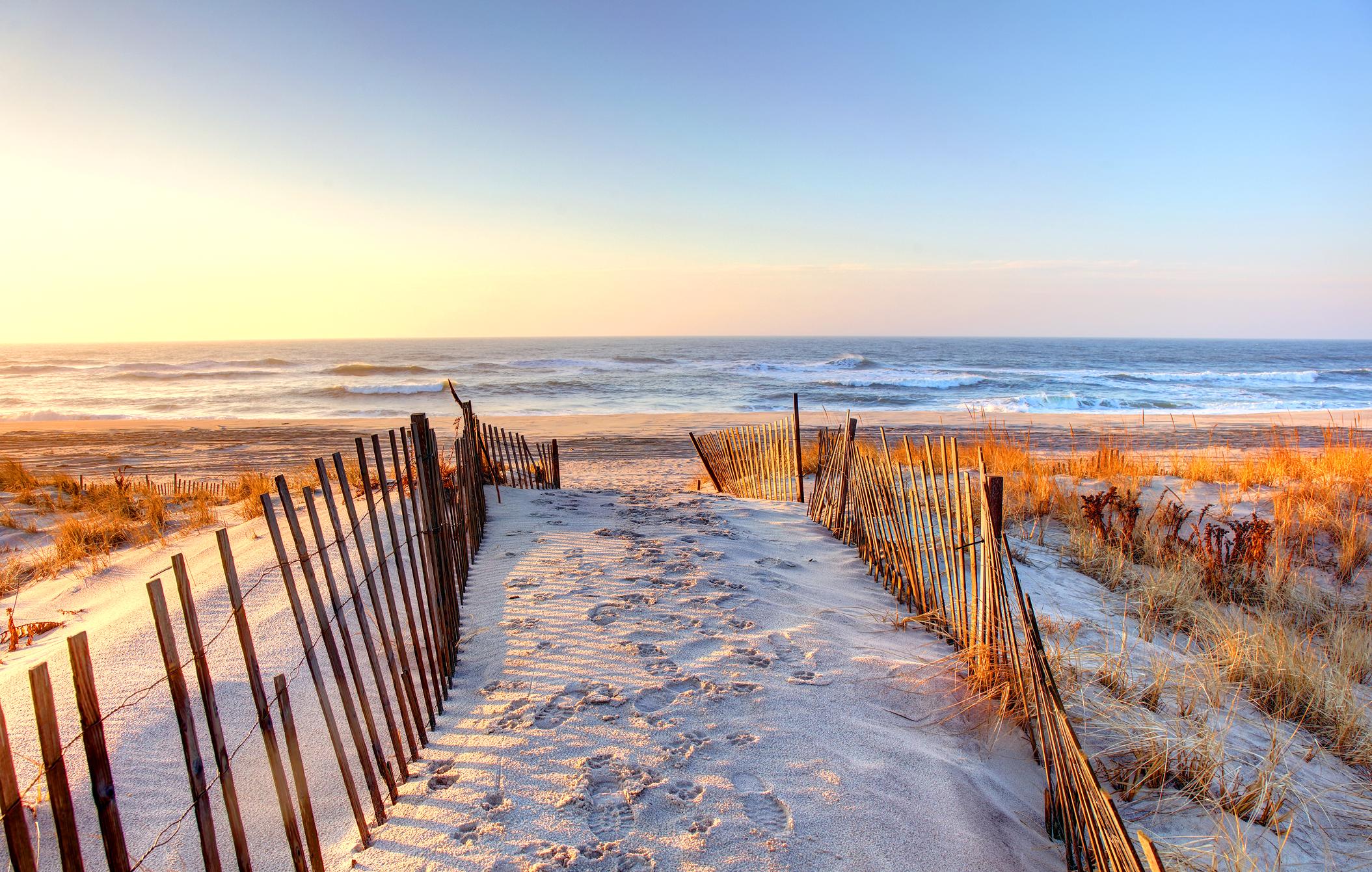 Scenic Hamptons beach pathway with wooden fences leading to the ocean at sunset